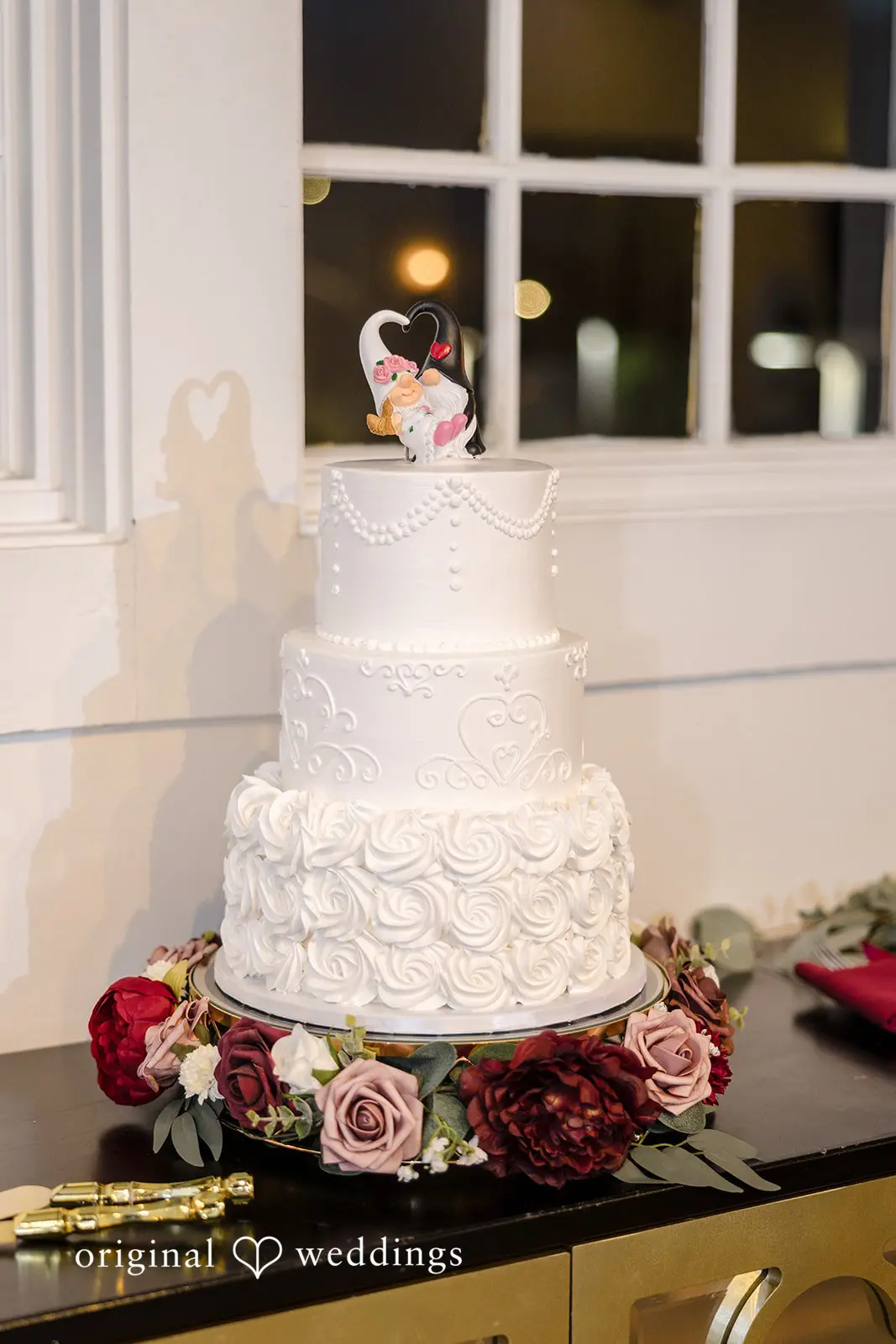 An all-white cake decorated with vibrant blooms at the wedding reception