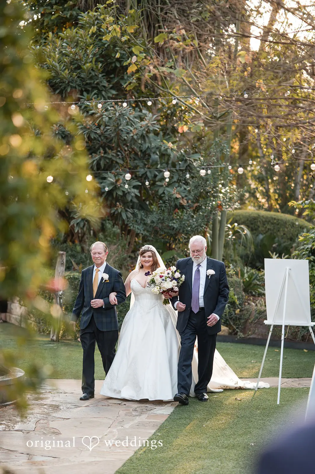 Ashley + David The bride is being escorted down the aisle