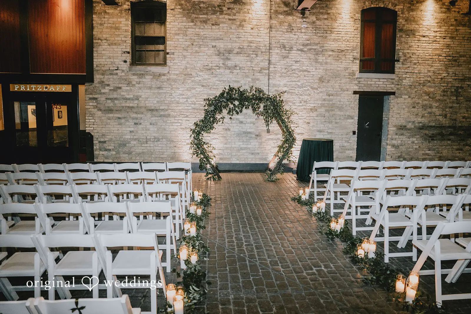 Hayden + Abby Indoor ceremony aisle with white chairs and a floral arch set up at Pritzlaff Events