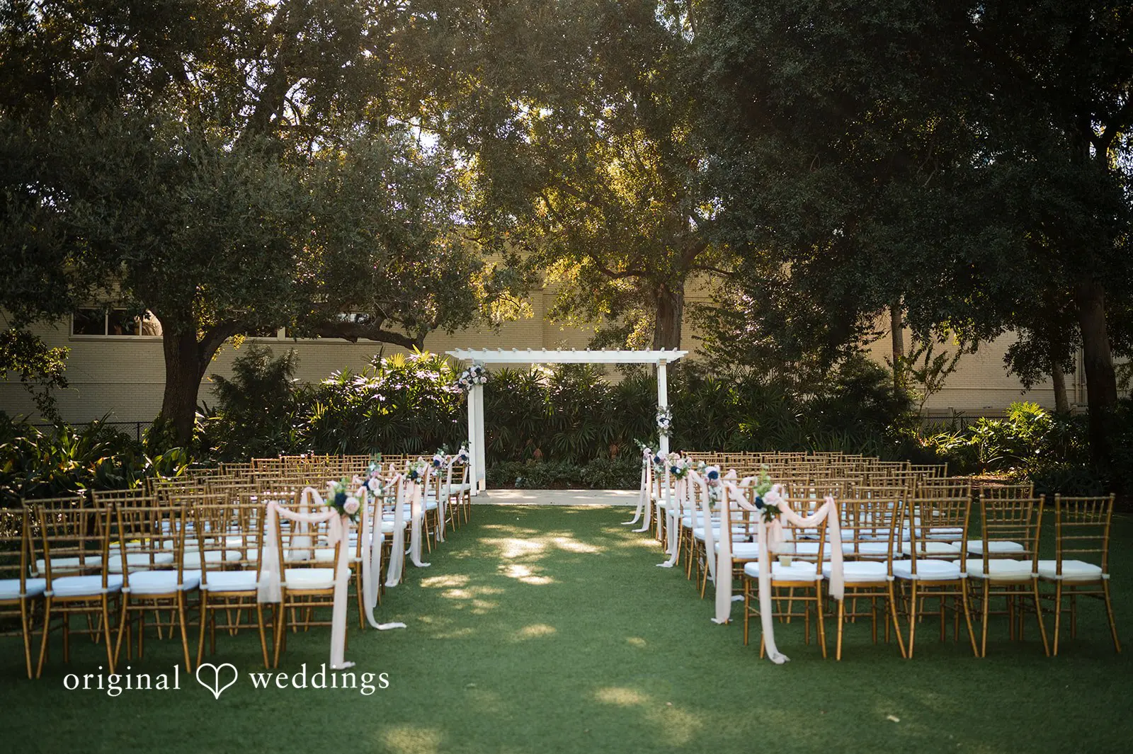 Outdoor ceremony aisle with white chairs and a floral arbor set up at Tampa Garden Club