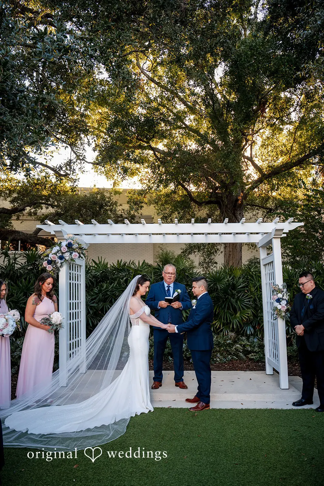 Bride and groom standing under white ceremony arbor