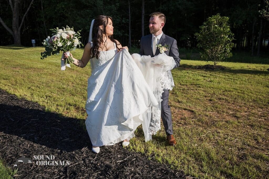 The groom helps carry the bride's train at The Oakley on the Lake Wedding