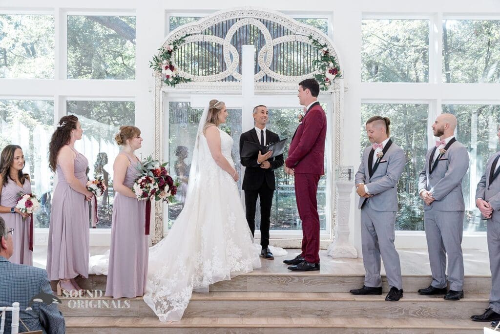 Bridesmaids and groomsmen in awe as bride and groom exchange marital vows at The French Farmhouse Wedding altar