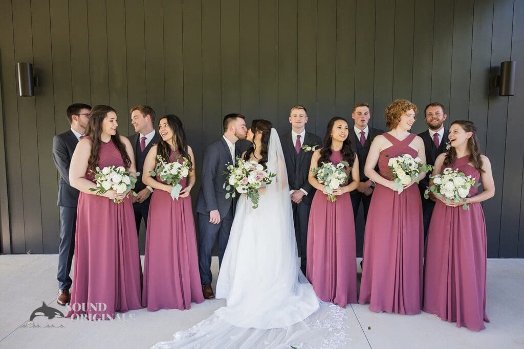 Bride and groom share a kiss in the presence of their bridal party at The Oakley on the Lake Wedding