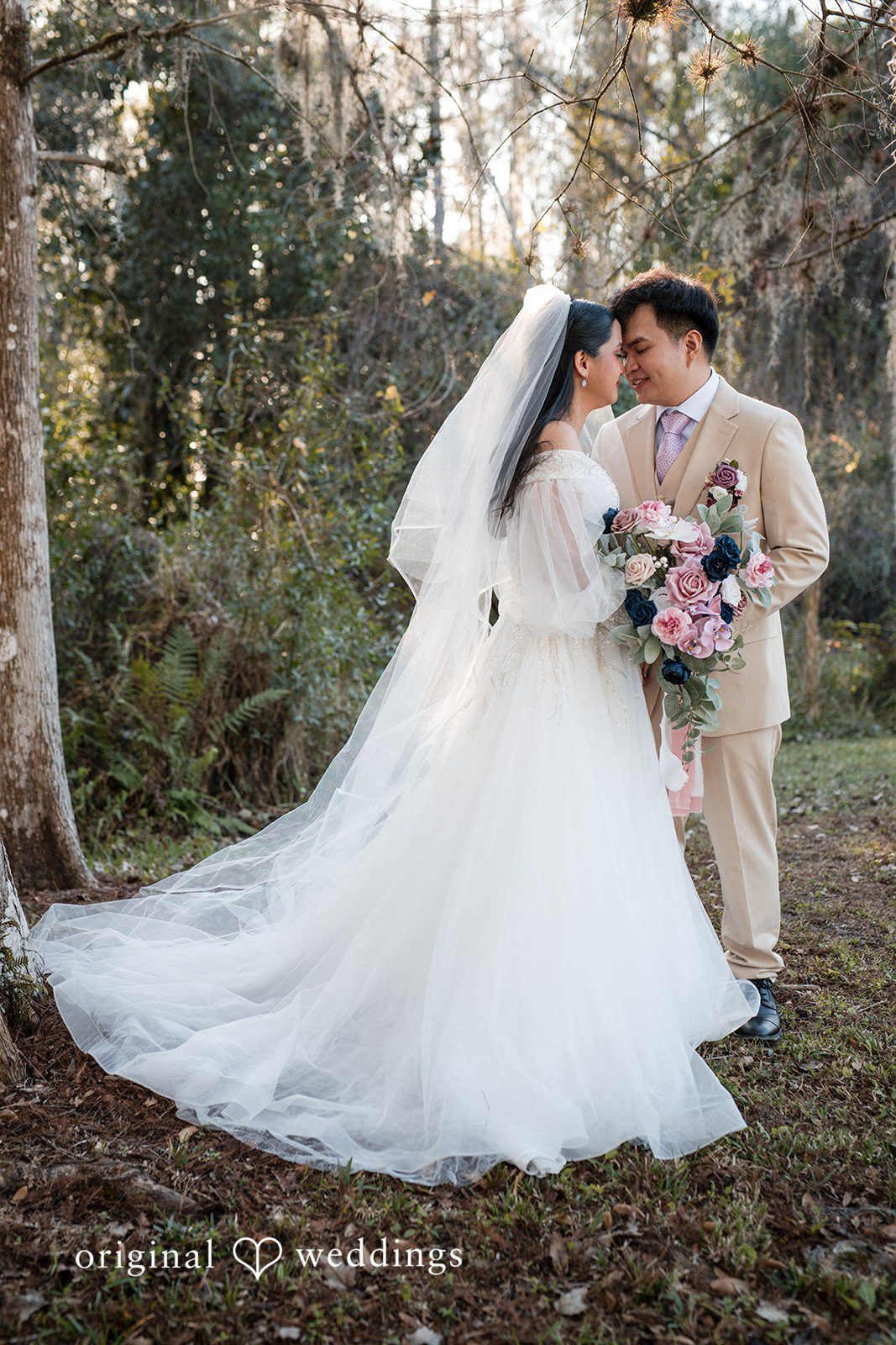 Andrea Edna + Canh Bride in white veil with groom at an outdoor wedding ceremony.