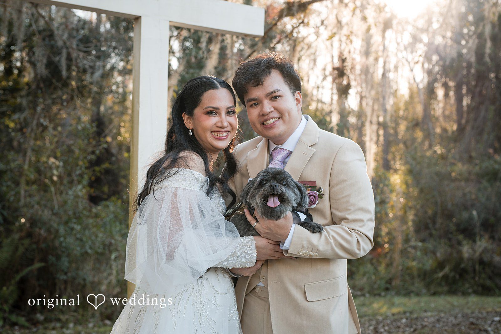 Andrea Edna + Canh Bride and groom holding a dog in wedding outfits.