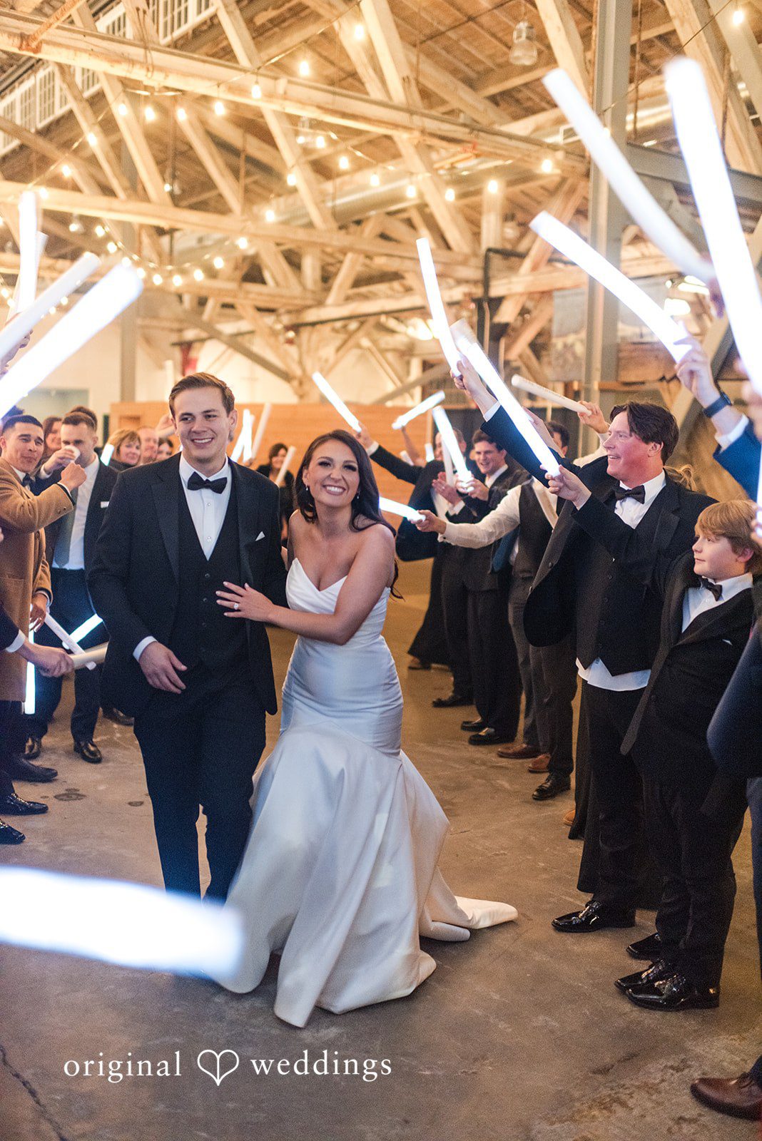 Kristi + Andrew Bride and groom smiling as they walk through guests holding glowing light sticks