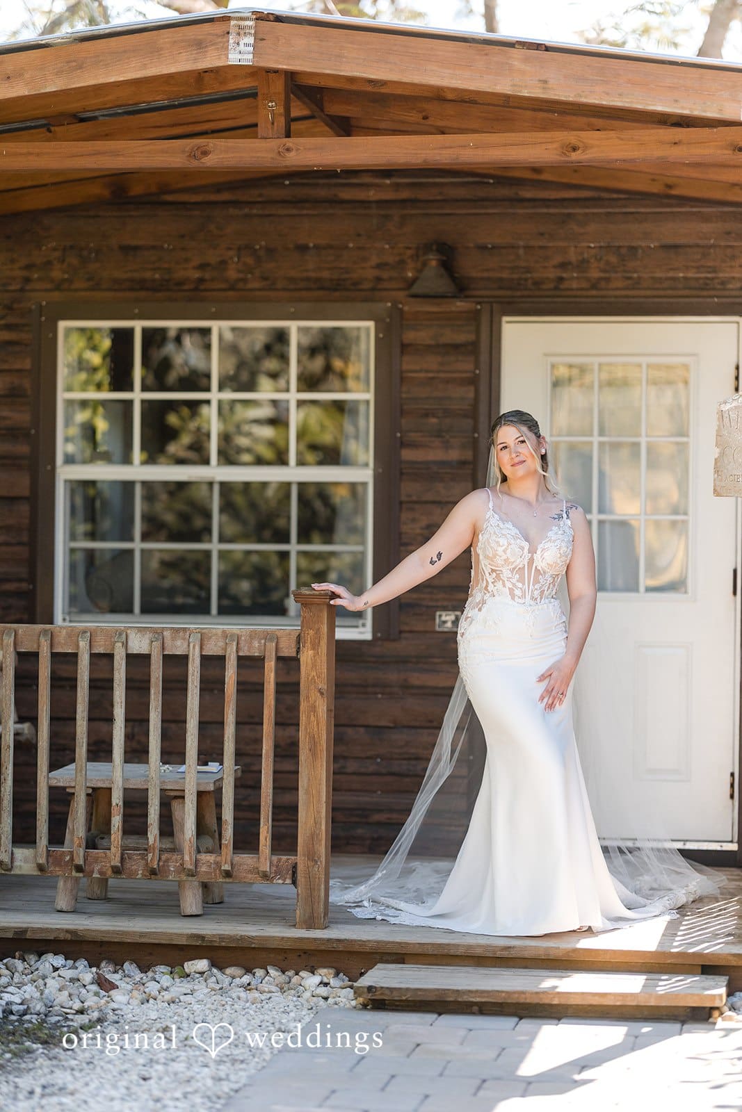 Bride standing near a wooden cabin doorway .