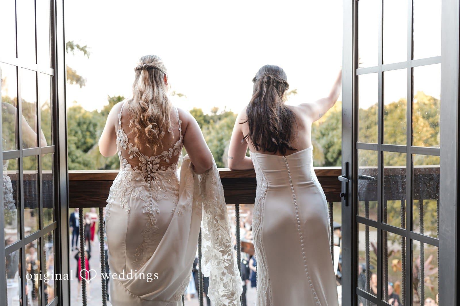 Two brides together outdoors in wedding attire.