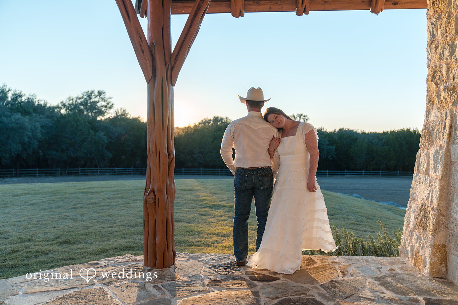 Standing under a rustic structure, they hold each other close.