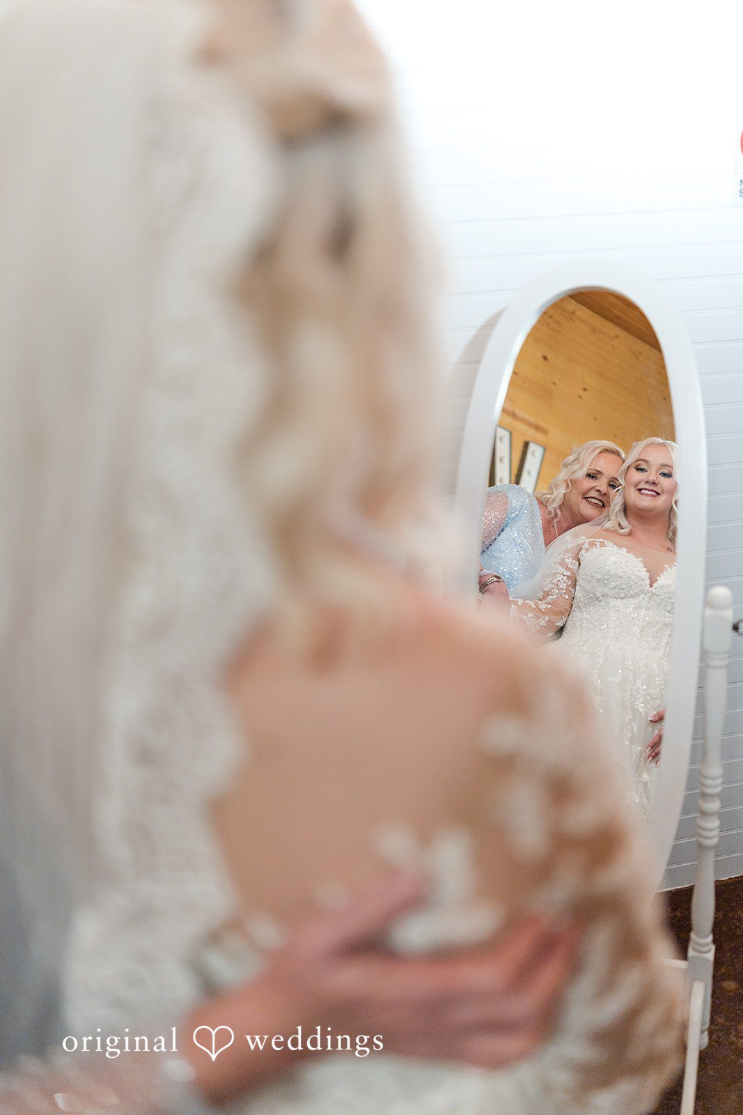 Elegant bride standing infront of mirror with someone at Lovely Barn