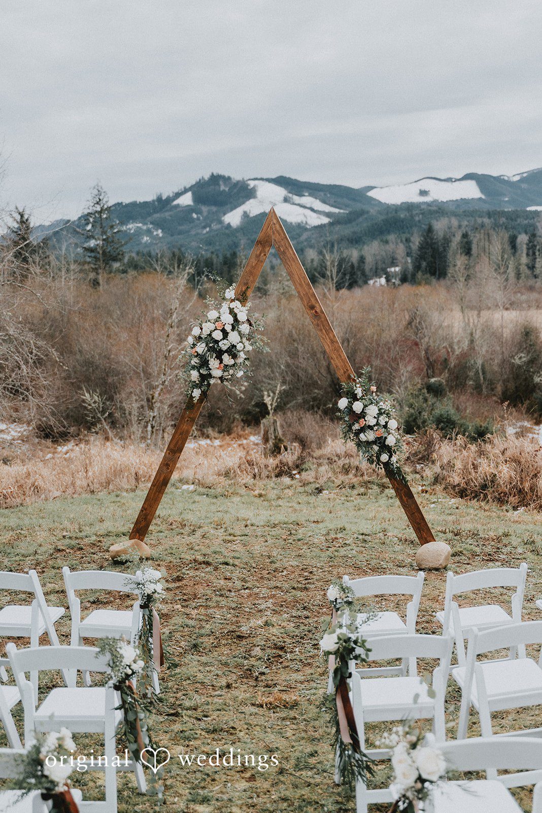 Kelsey + Adam Wedding ceremony arch with chairs set up in an open field.