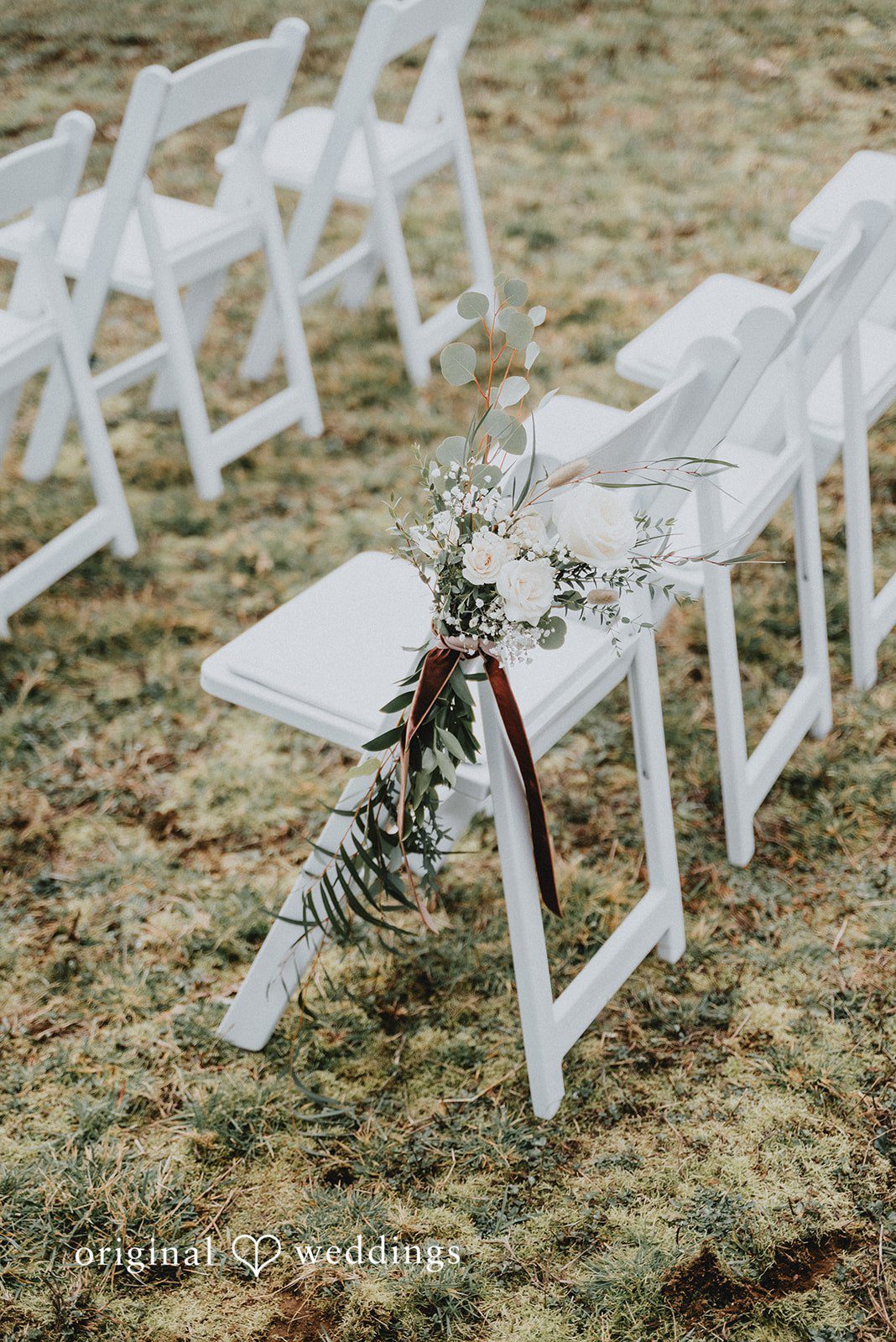 Kelsey + Adam Close-up of ceremony seating aisle with white chairs.