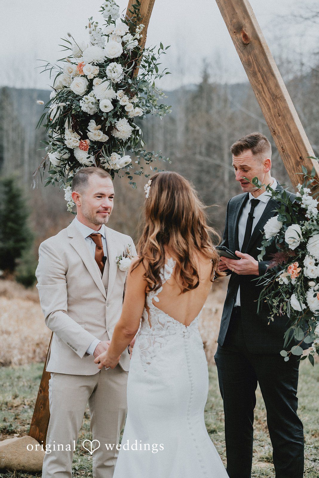 Kelsey + Adam Bride, groom & officiant at outdoor wedding arch with mountains.