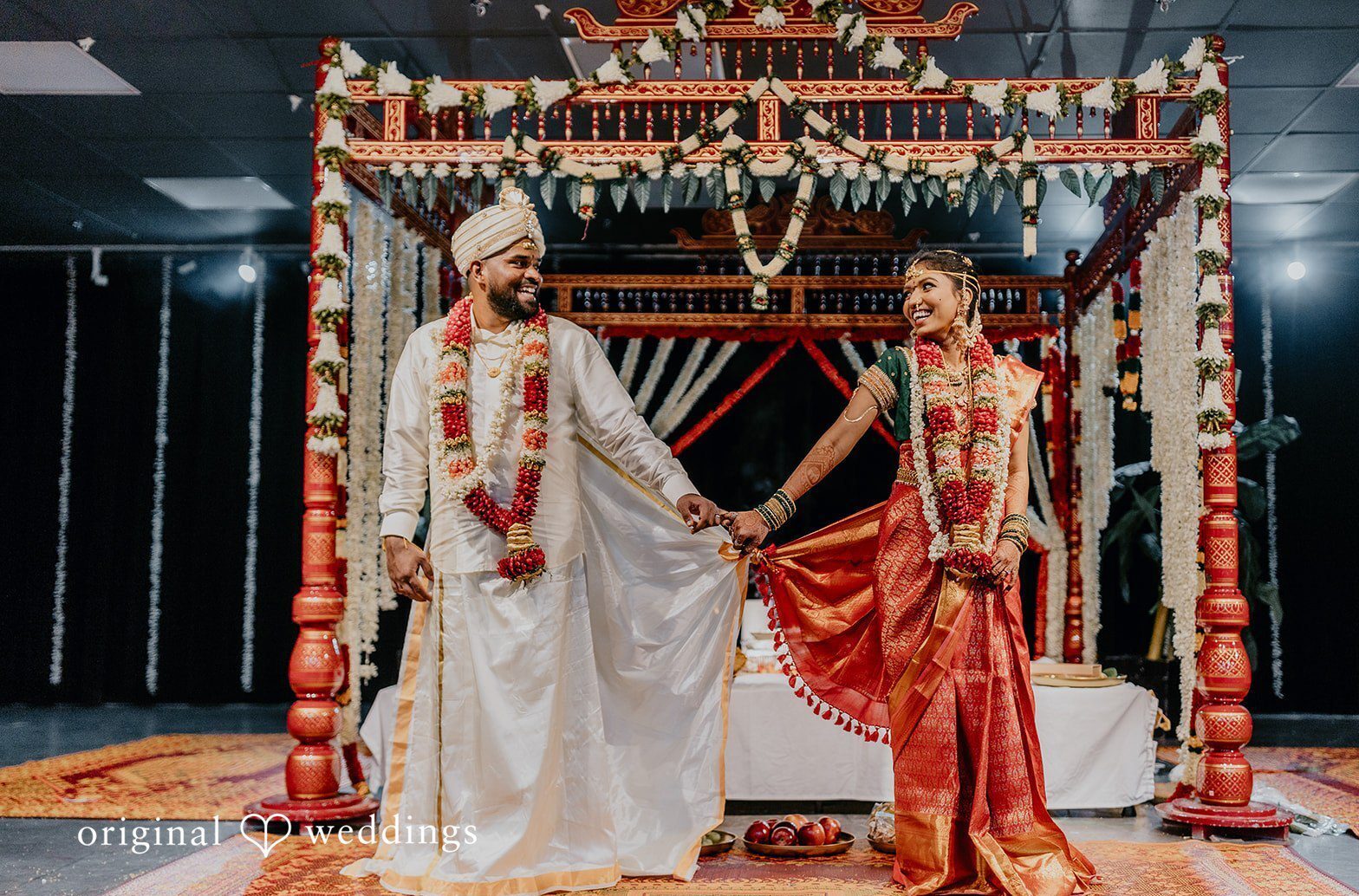 A couple walking hand in hand beneath an ornate ceremonial canopy, showcasing detailed attire and traditional decor, captured in a refined Baltimore wedding photography style that highlights elegance and cultural details.