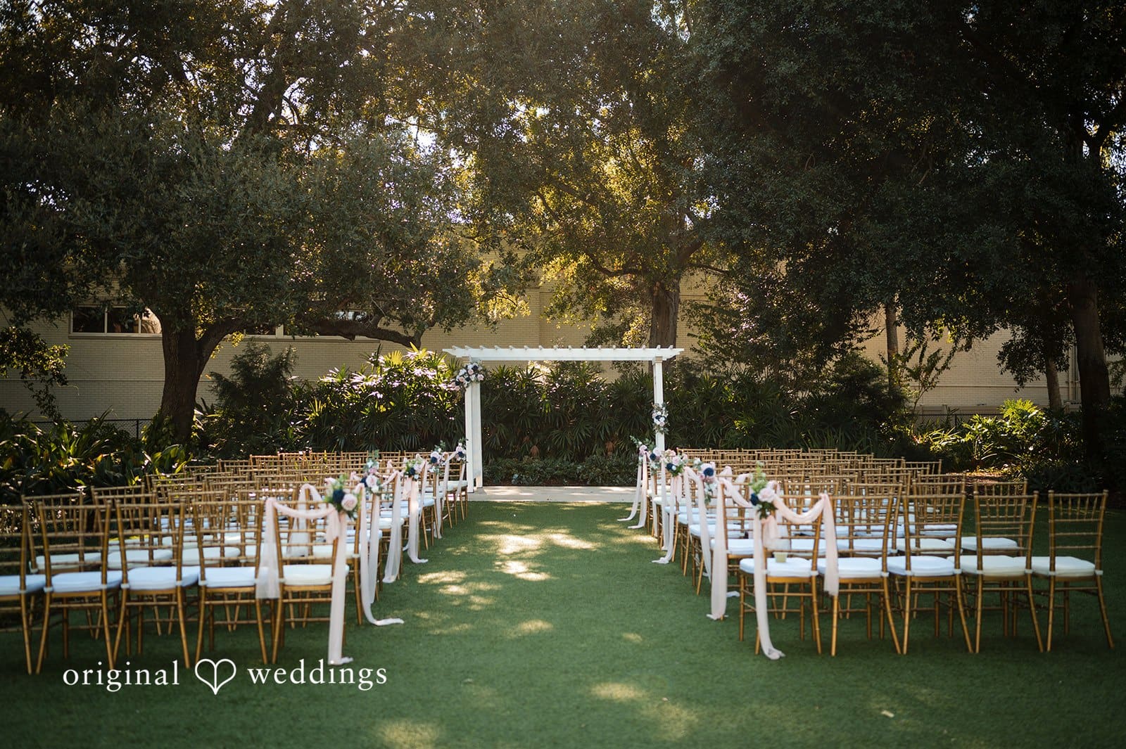 Outdoor ceremony aisle with white chairs and a floral arbor set up at Tampa Garden Club