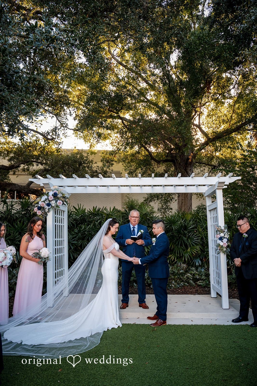Bride and groom standing under white ceremony arbor