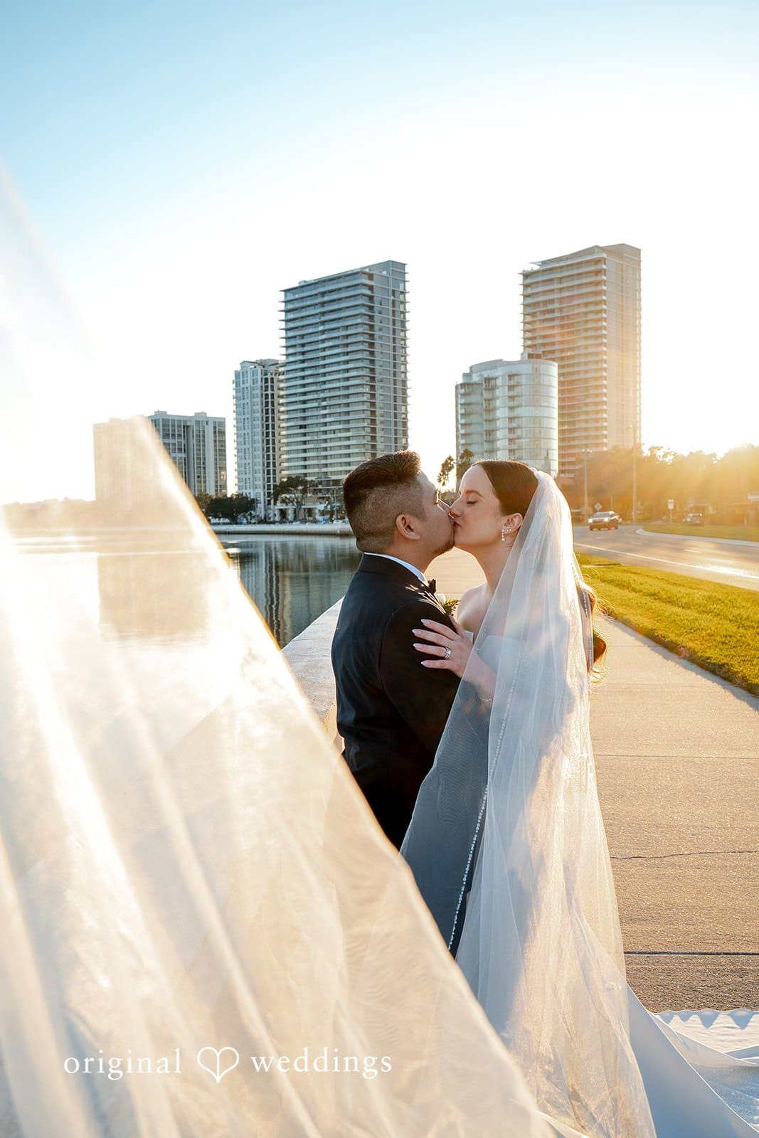 Bride and groom sharing a kiss by the waterfront at Tampa Garden Club during golden hour with the Tampa skyline in the background