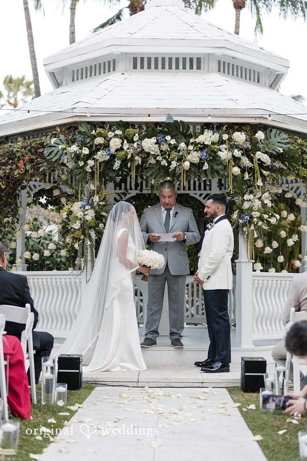 Couple standing before the priest, looking at each other at The Palms Hotel & Spa