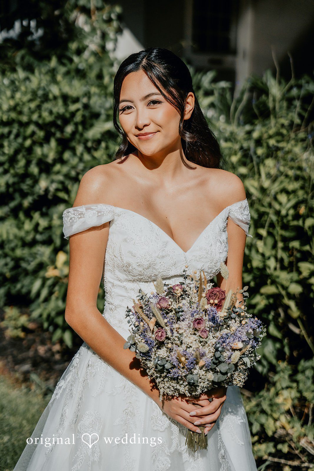 The bride smiles gracefully while holding her bouquet.