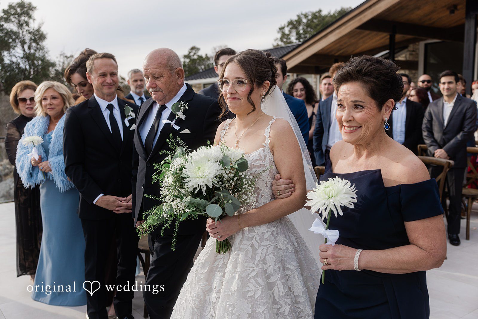 The bride's parents joyfully walk the bride down the aisle