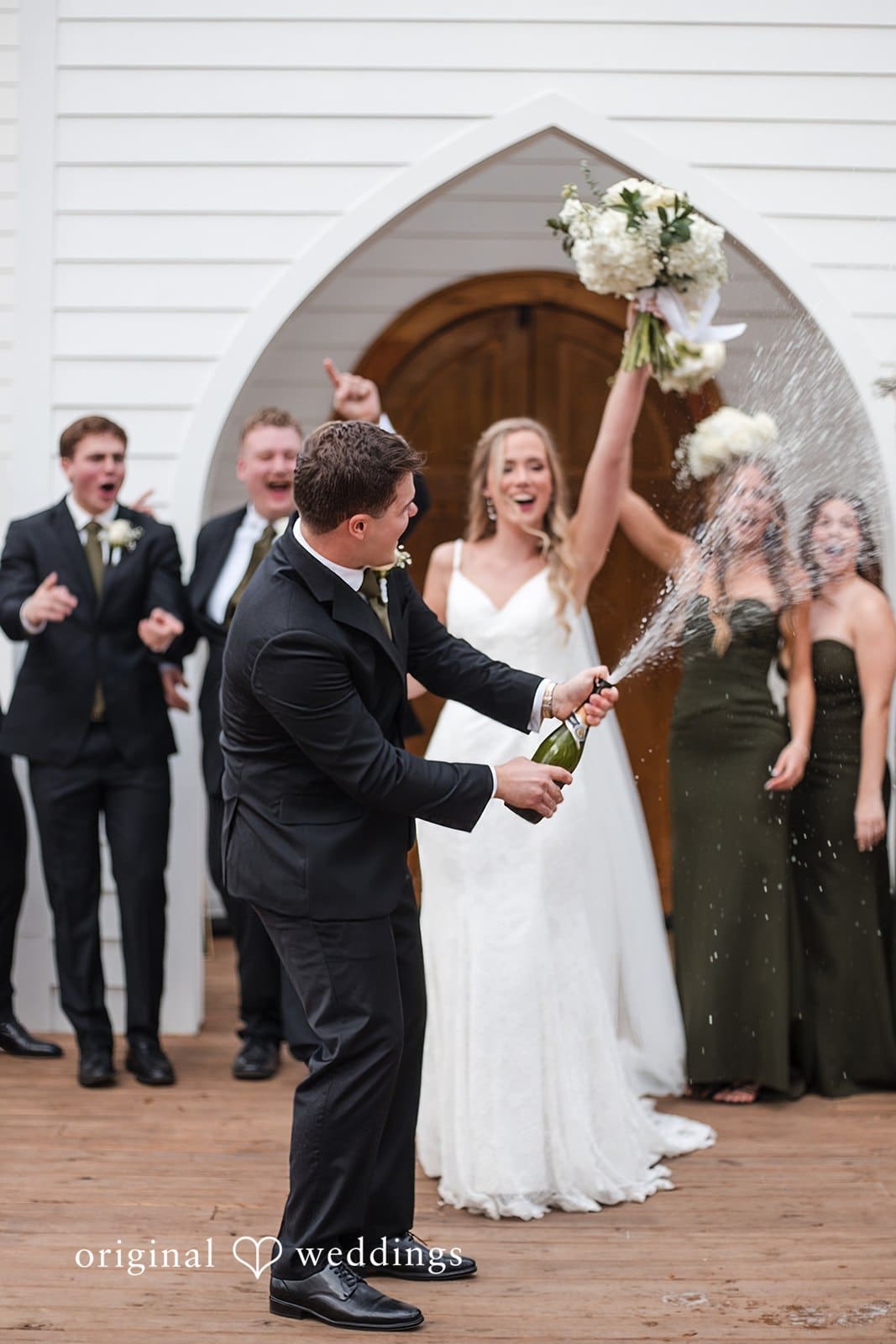 January 03, 2026 – Brianne & Luke – (ID-4948) Groom opens a wine bottle while bride laughs joyfully at wedding celebration