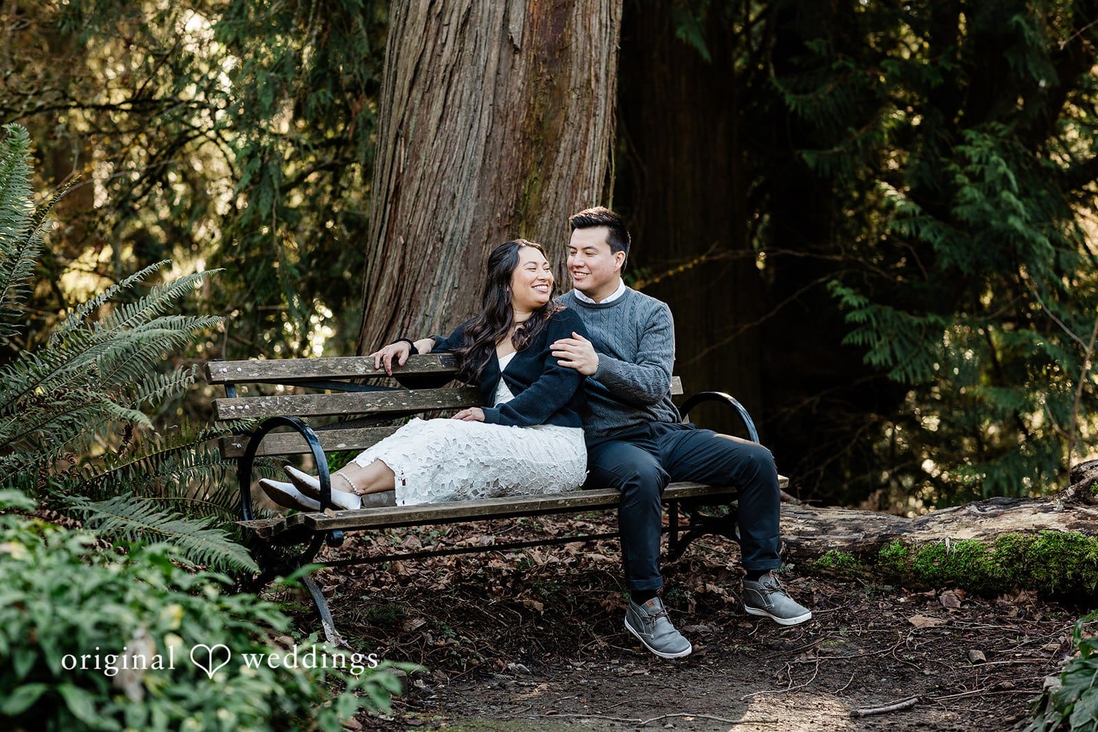 Romantic engagement photo of couple on a bench with groom seated behind the bride at Washington Park Arboretum