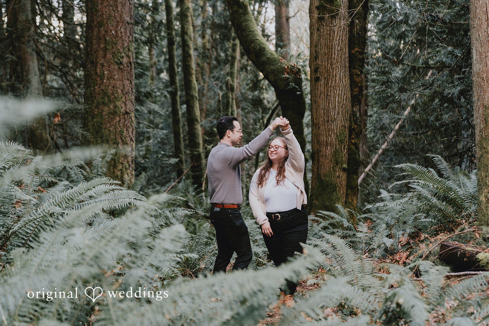 Couple in a forest engagement shoot, man lifting woman’s hand..