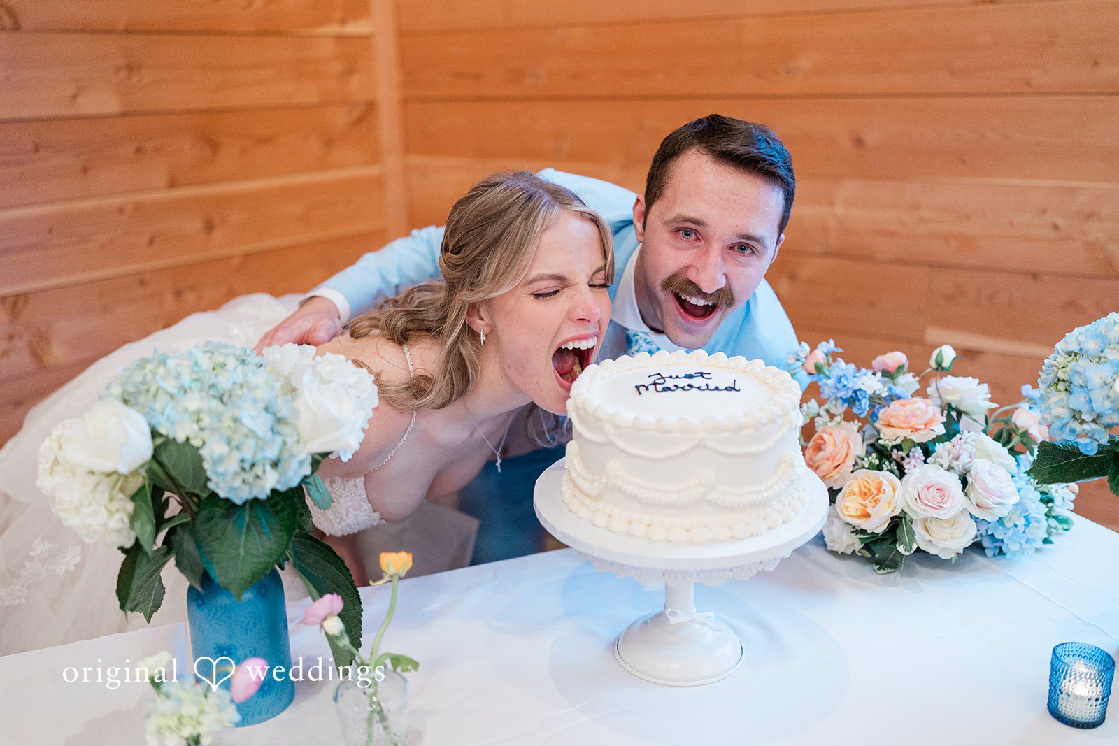 Aubrey + Casey The bride playfully takes a bite of the wedding cake while the groom laughs beside her.