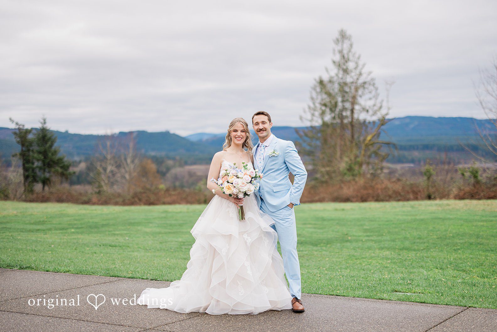 The couple stands together outdoors, posing with a scenic mountain view, capturing the essence of Seattle wedding photography.