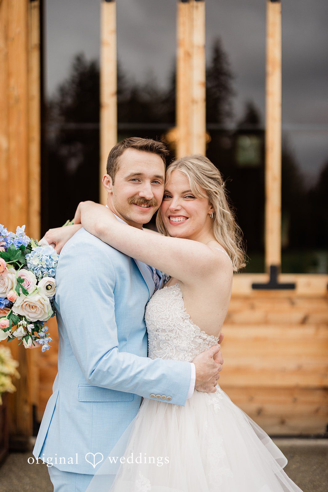 Aubrey + Casey The couple embraces lovingly in front of a rustic wooden backdrop.