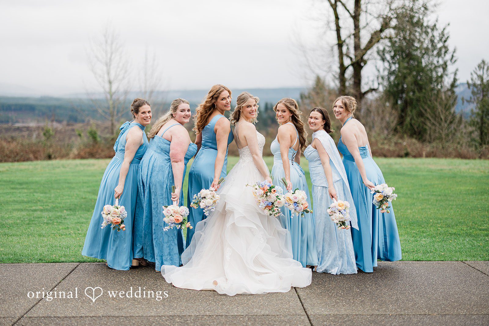 Aubrey + Casey The bride stands with her bridesmaids dressed in matching blue gowns outdoors.