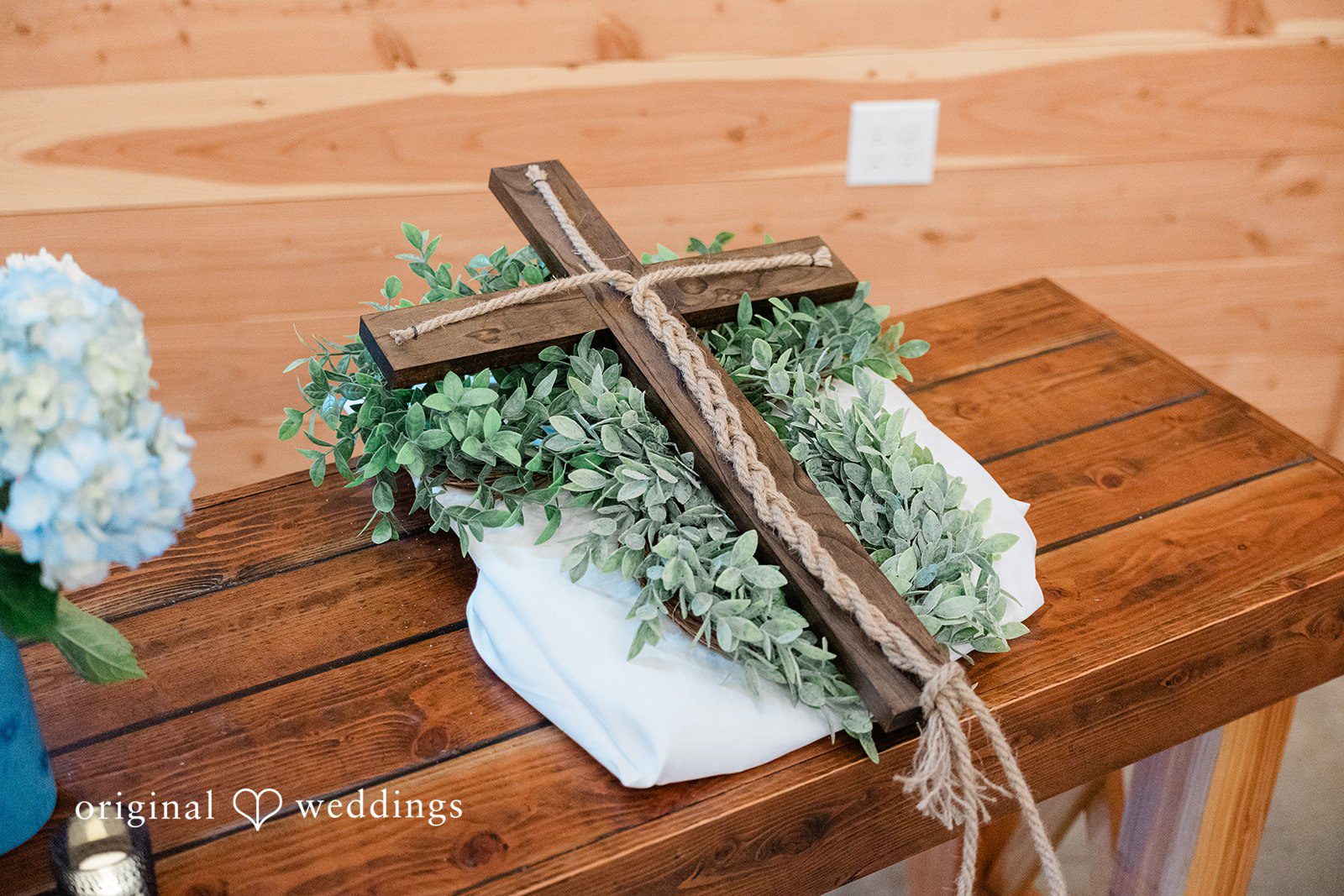 Aubrey + Casey Wedding décor with a cross and greenery is displayed beautifully on a wooden table.