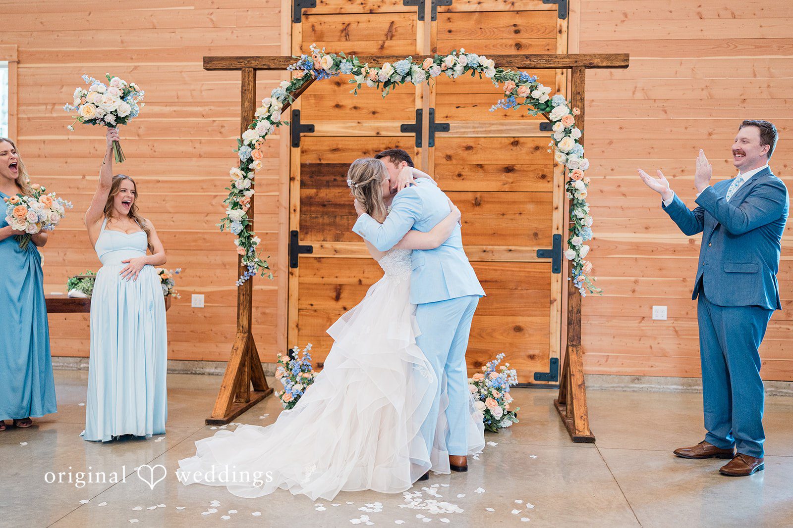Aubrey + Casey The couple shares a kiss under a floral arch while guests applaud.