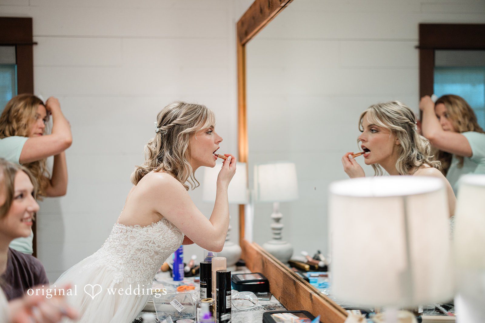 Aubrey + Casey The bride smiles while getting ready in front of the mirror with her friends.
