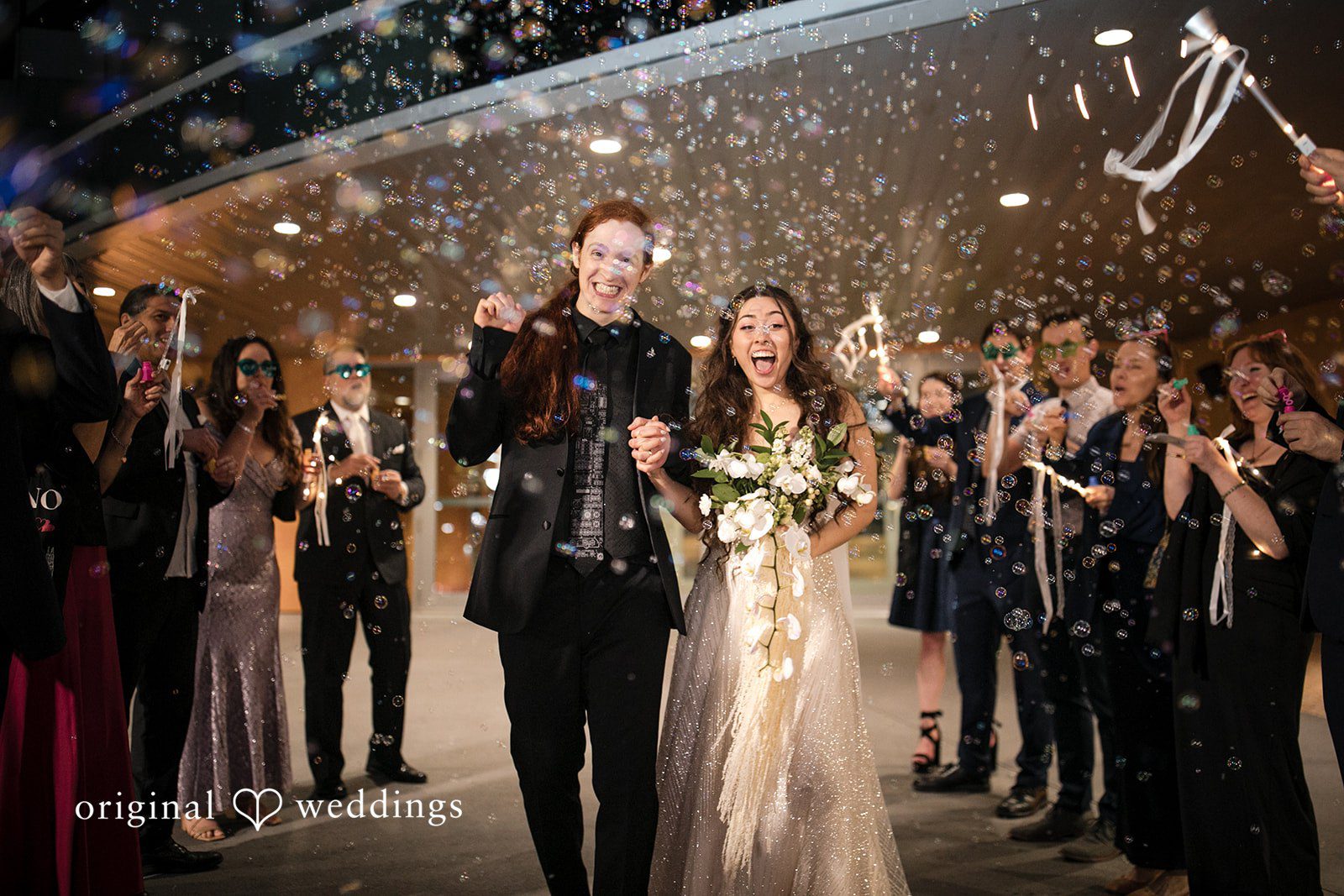Bride and groom walking hand in hand through guests blowing bubbles