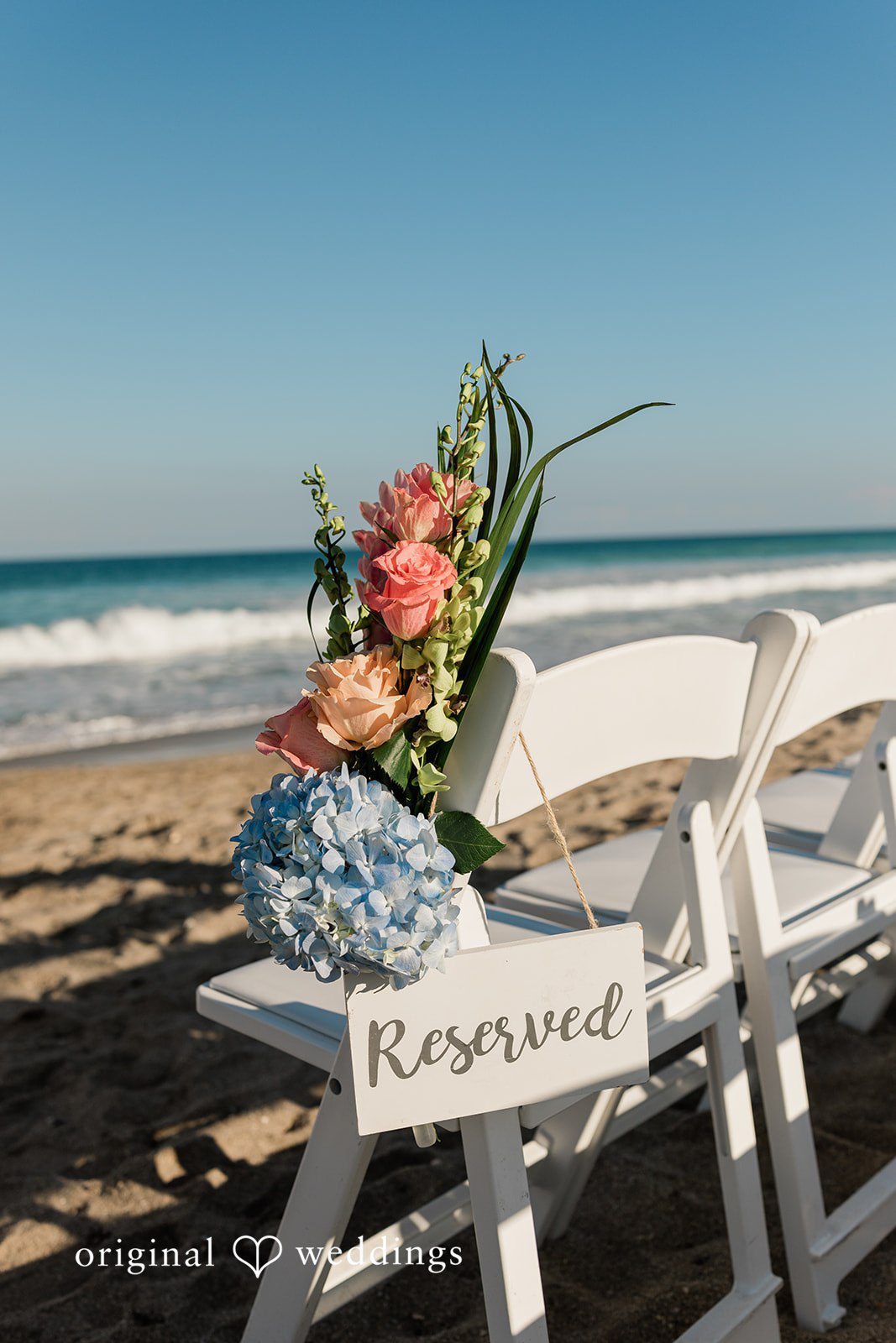 Ethan + Sydney Reserved chair with floral arrangement by the beach.