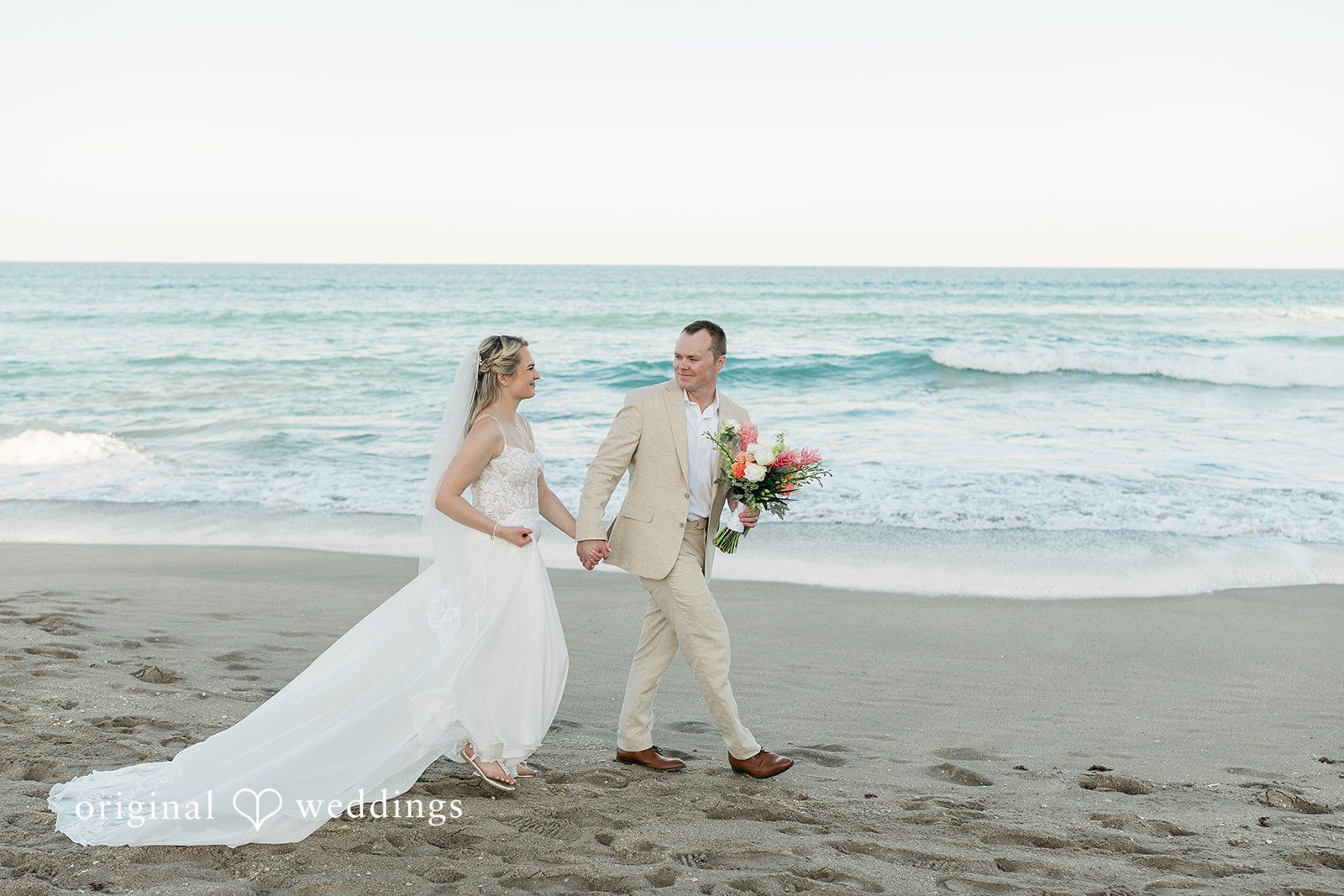 Ethan + Sydney Couple walking along shoreline in wedding attire.