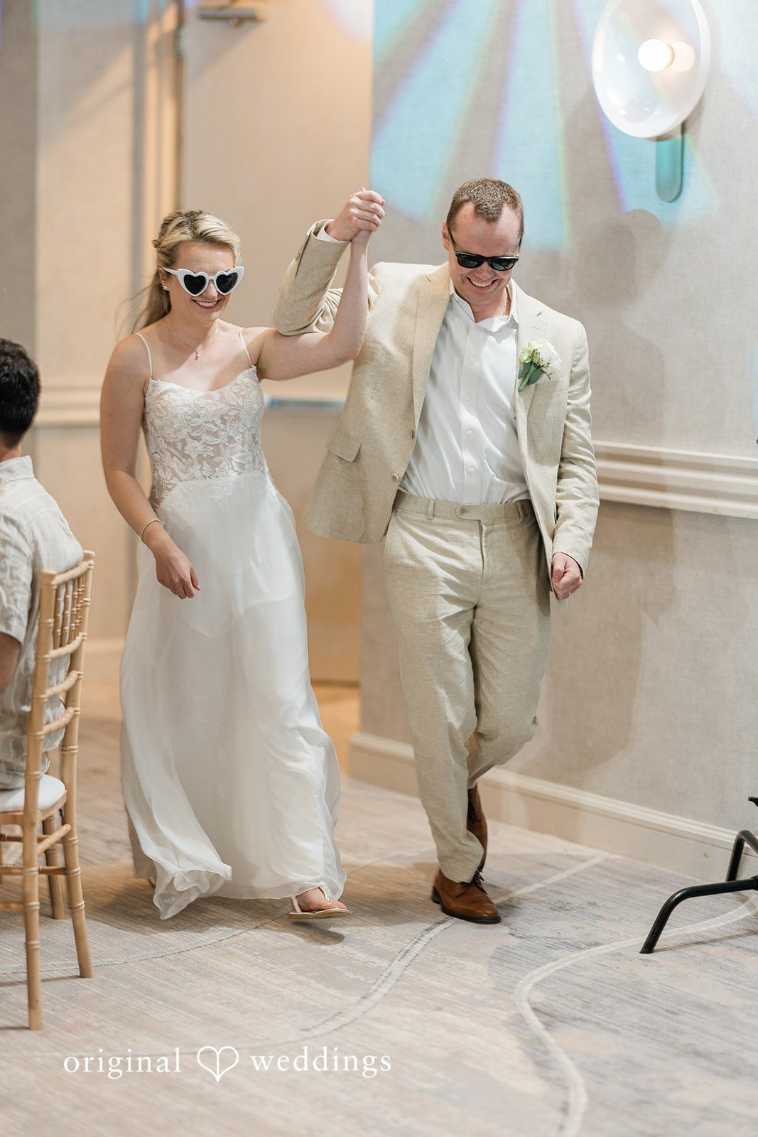 Ethan + Sydney Couple walking hand-in-hand down an aisle, wearing sunglasses.