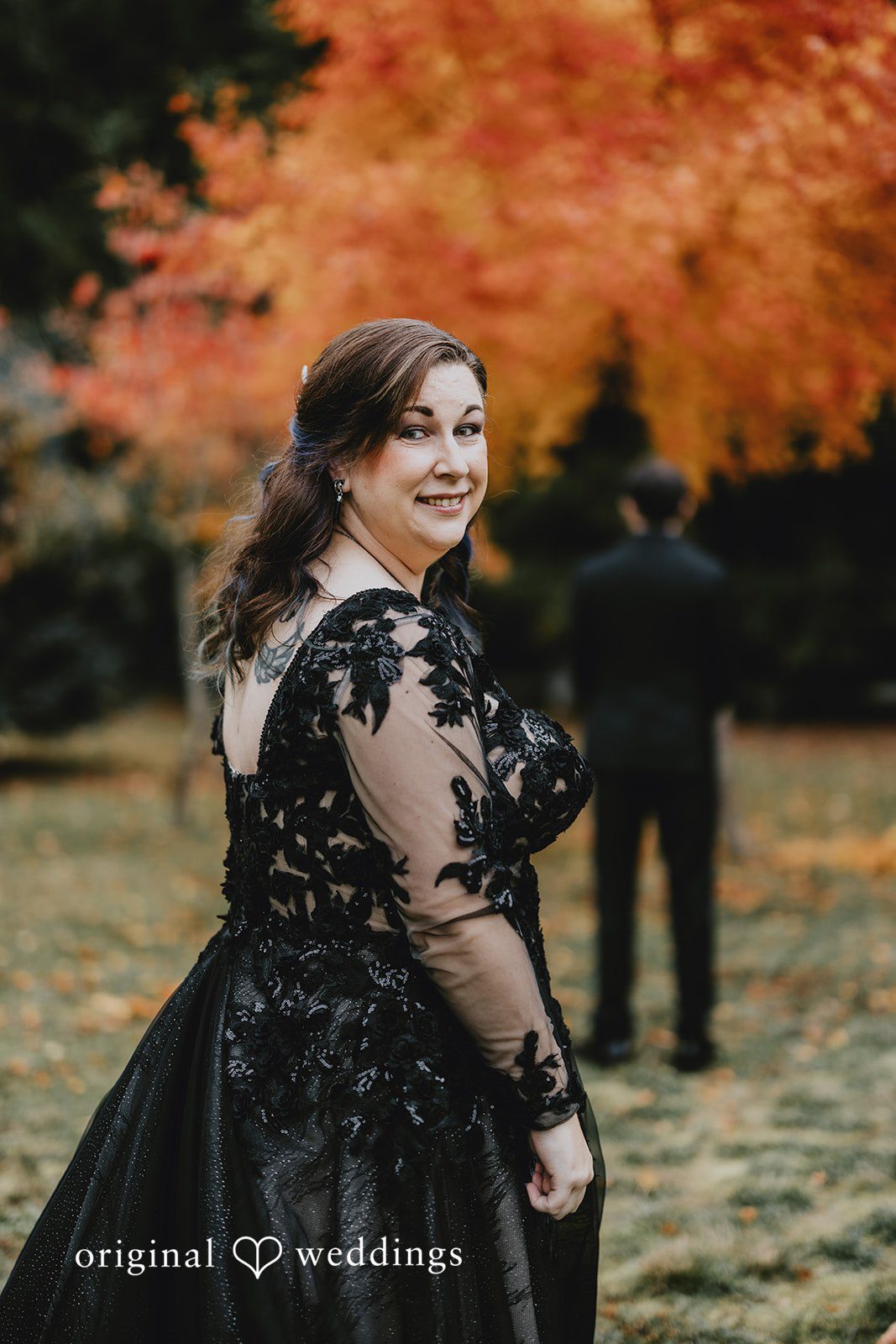 Two people walking along a gravel path are framed by trees and open space.