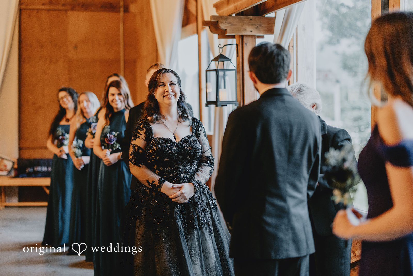 Two people facing each other indoors are framed by guests observing the ceremony.