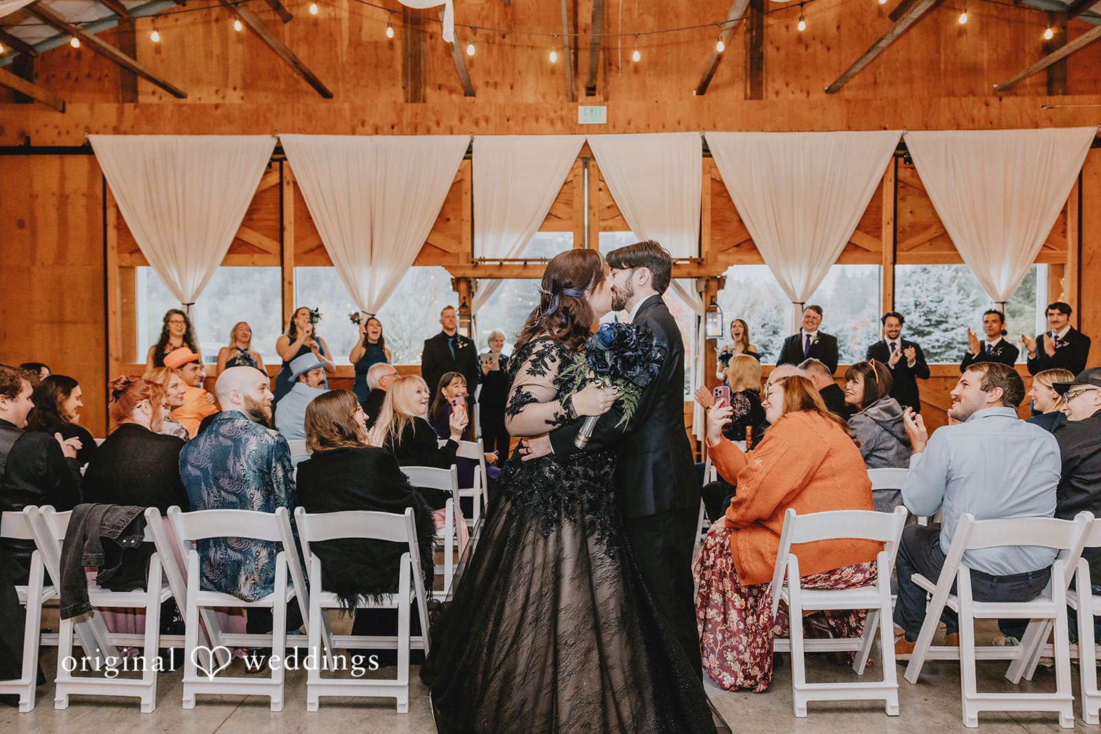 A wedding party walking between chairs inside a wooden venue captures the start of the ceremony in a documentary style.