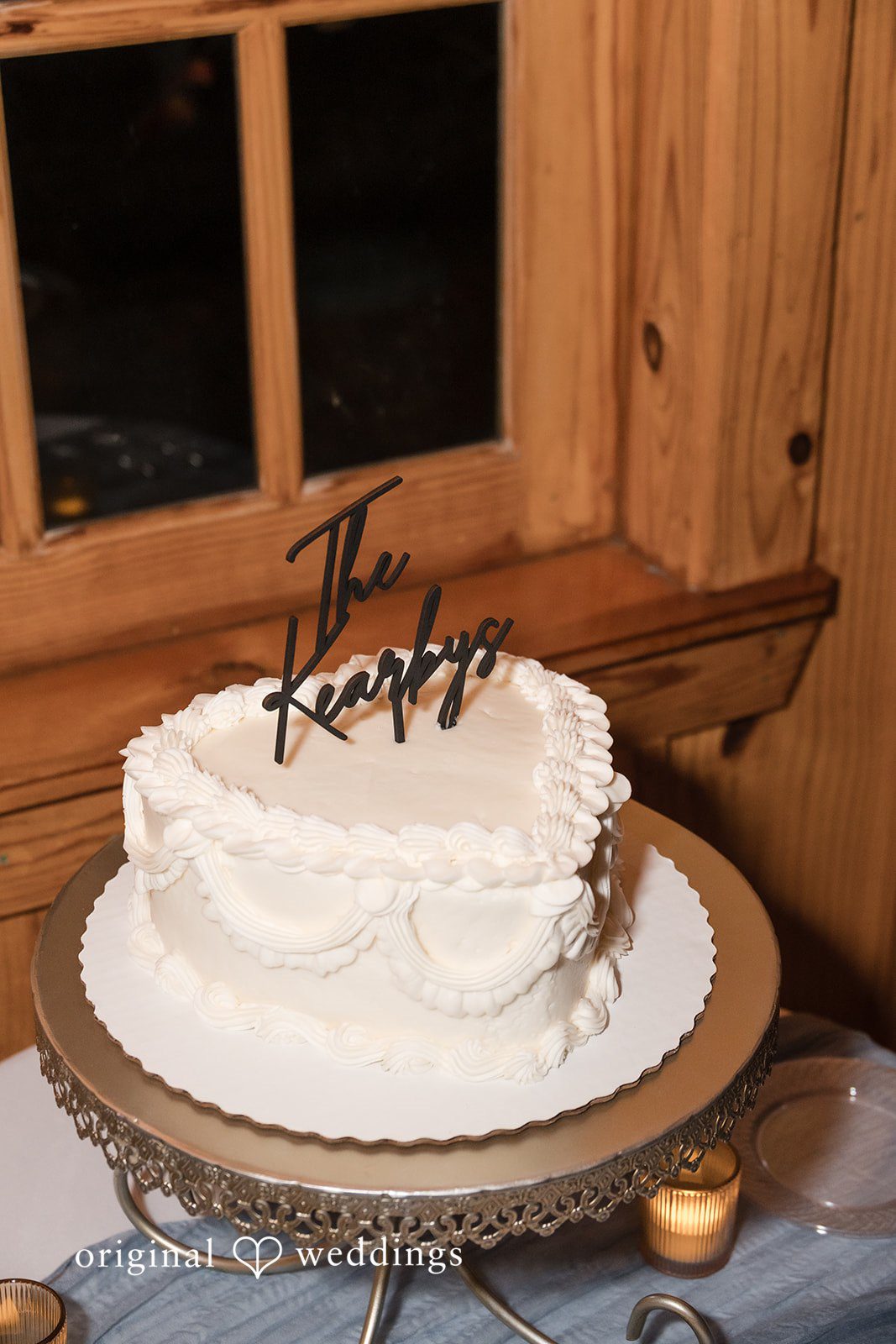 Kelsey + Riley A white wedding cake with elegant details sits on a wooden table.