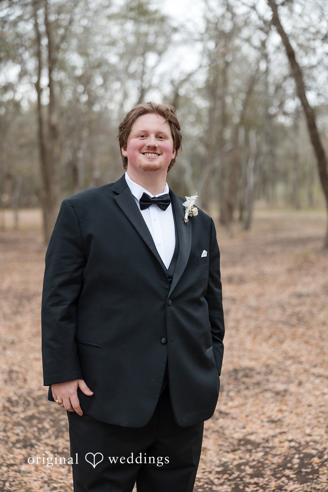 Kelsey + Riley The groom stands alone outdoors in a formal black suit.