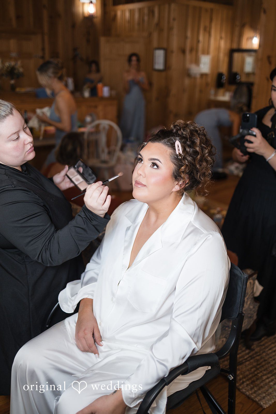 Kelsey + Riley A bride gets her makeup done while sitting indoors.