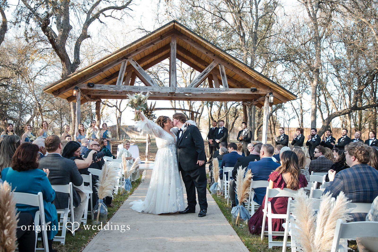 Kelsey + Riley Guests watch as the couple stands together under a wooden arch.