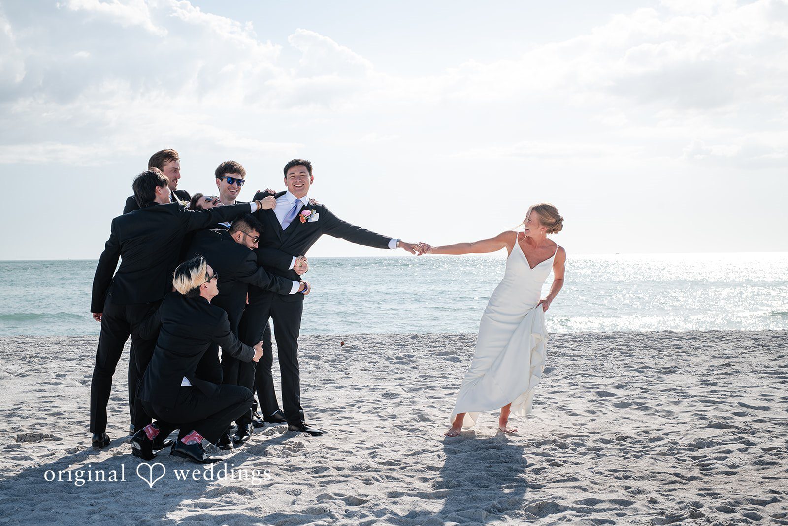 Wedding photo of groom holding bride’s hand while being playfully pulled by groomsmen at The Resort at Longboat Key Club