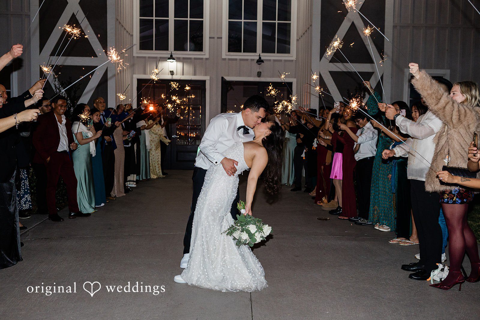 Dominic + Erika Joy Sparkler Send-off Kiss: A couple sharing a kiss while walking through a tunnel of guests at Addison Woods