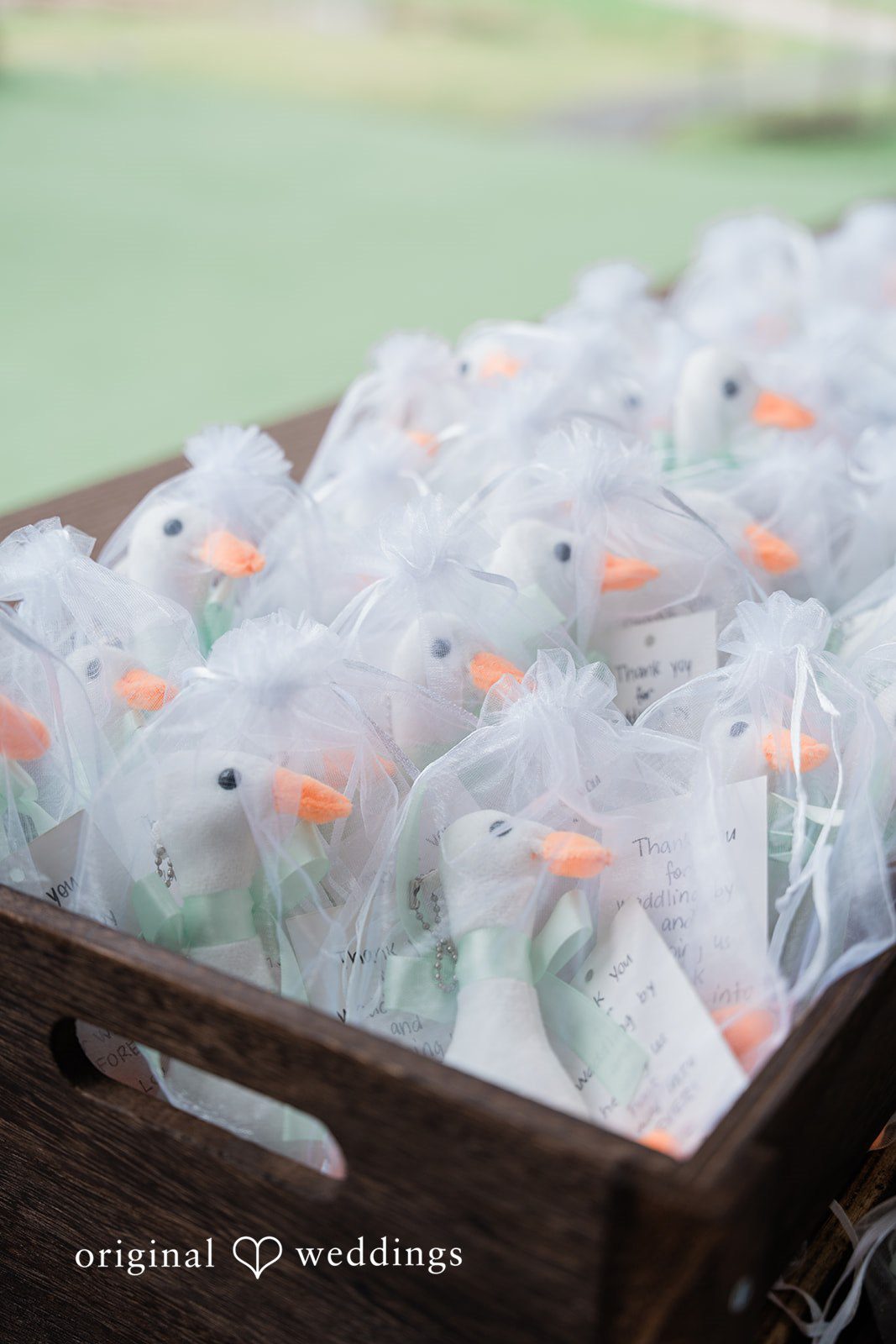 Dominic + Erika Joy A wooden crate filled with small, transparent favor bags containing white, round treats.