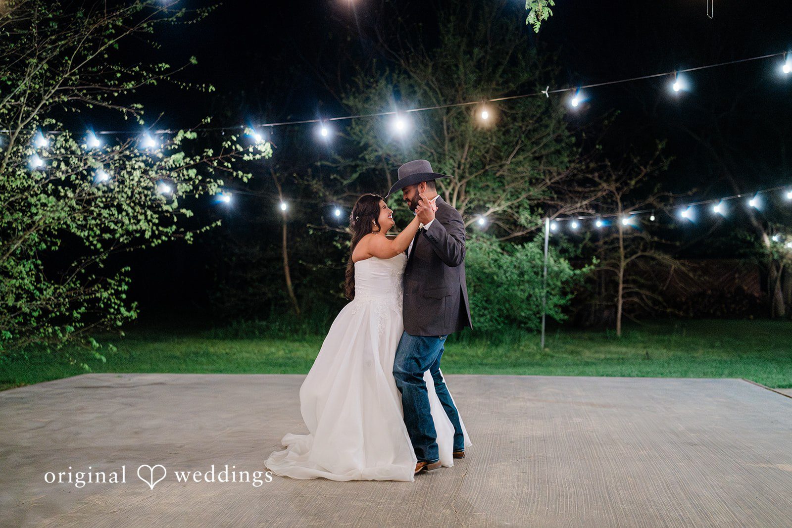 The couple dances outdoors under the string lights